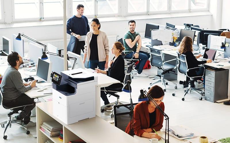 Eine Gruppe von Fachleuten, die in einem Büro zusammenarbeiten, Computer und den Xerox® VersaLink® B625 Multifunktionsdrucker für ihre Aufgaben nutzen.